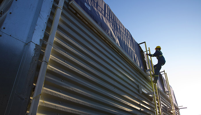 Two Carbon Engineering employees in blue coveralls take measurements outside at a direct air capture facility with mountains in the background and liquid nitrogen in the foreground.