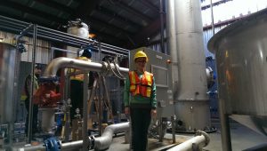 A Carbon Engineering employee stands in an orange reflective vest in front of some of the company's direct air capture equipment in a warehouse.
